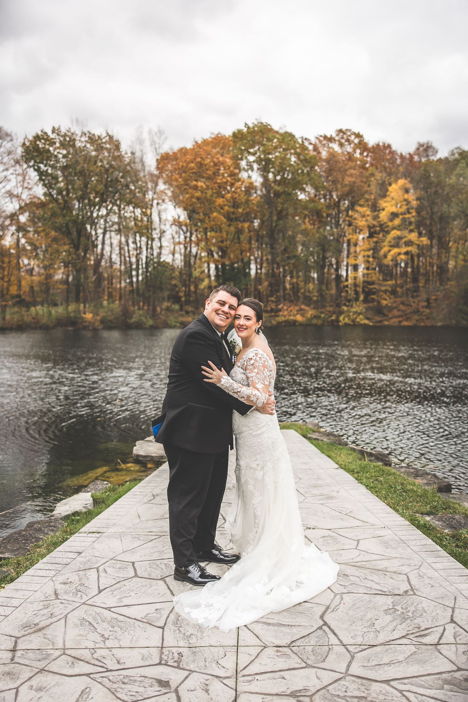 Newlyweds share intimate moments on stone terrace overlooking autumn lake.