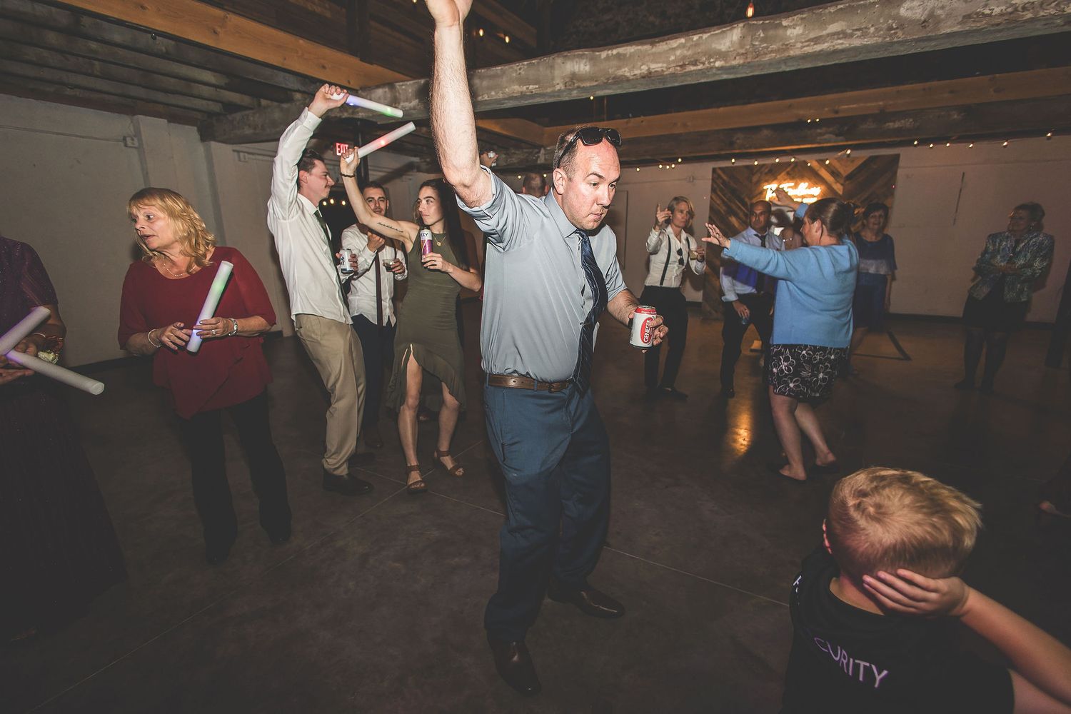 People dancing and celebrating at a wedding reception in a rustic indoor venue.