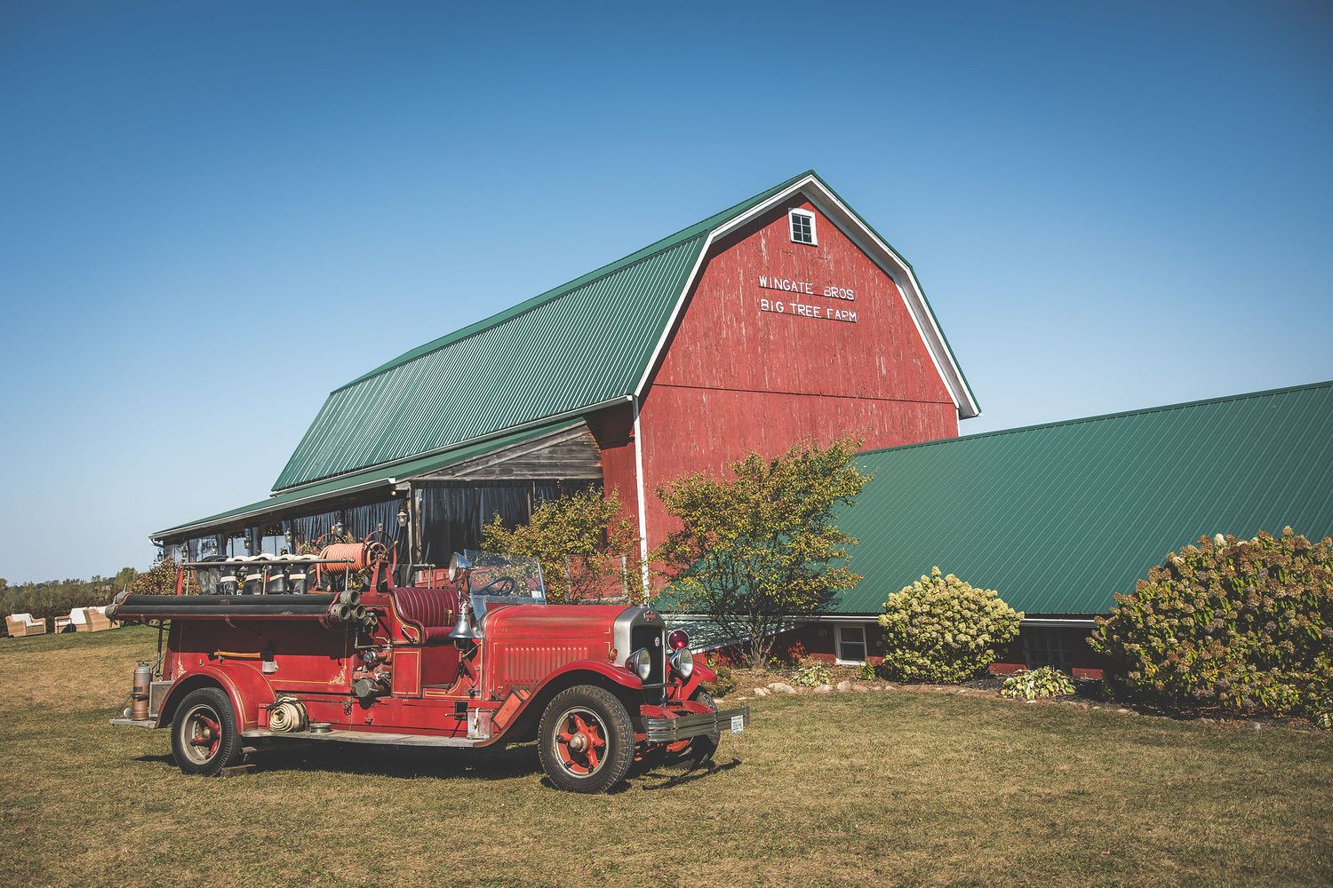 Panoramic view of a rustic red barn and farm buildings against a blue sky on a sunny day.