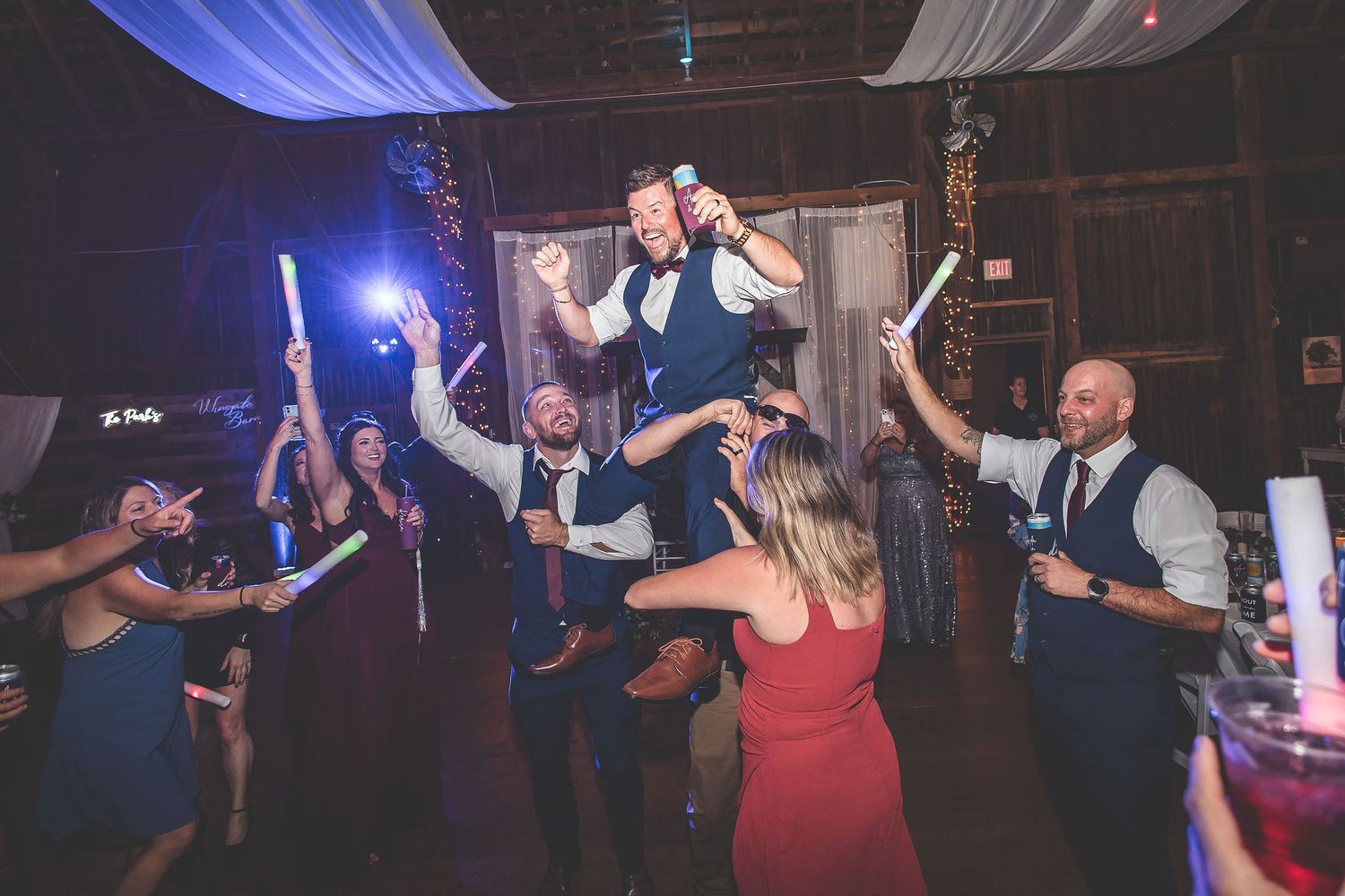 Wedding guests dancing under blue and white fabric draping in a rustic venue.