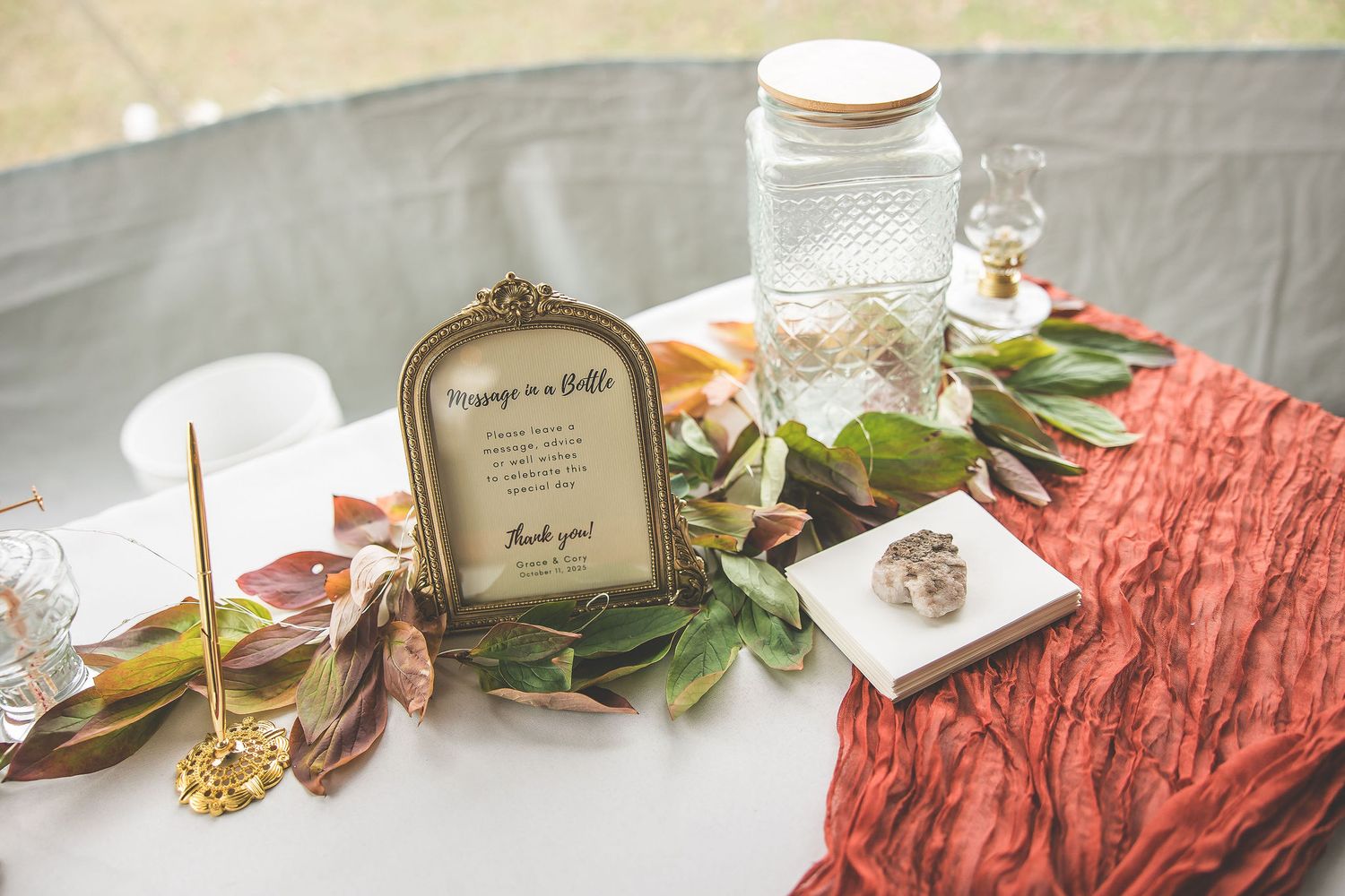 Wedding reception table details with place cards, greenery, and rustic decor on white linens.