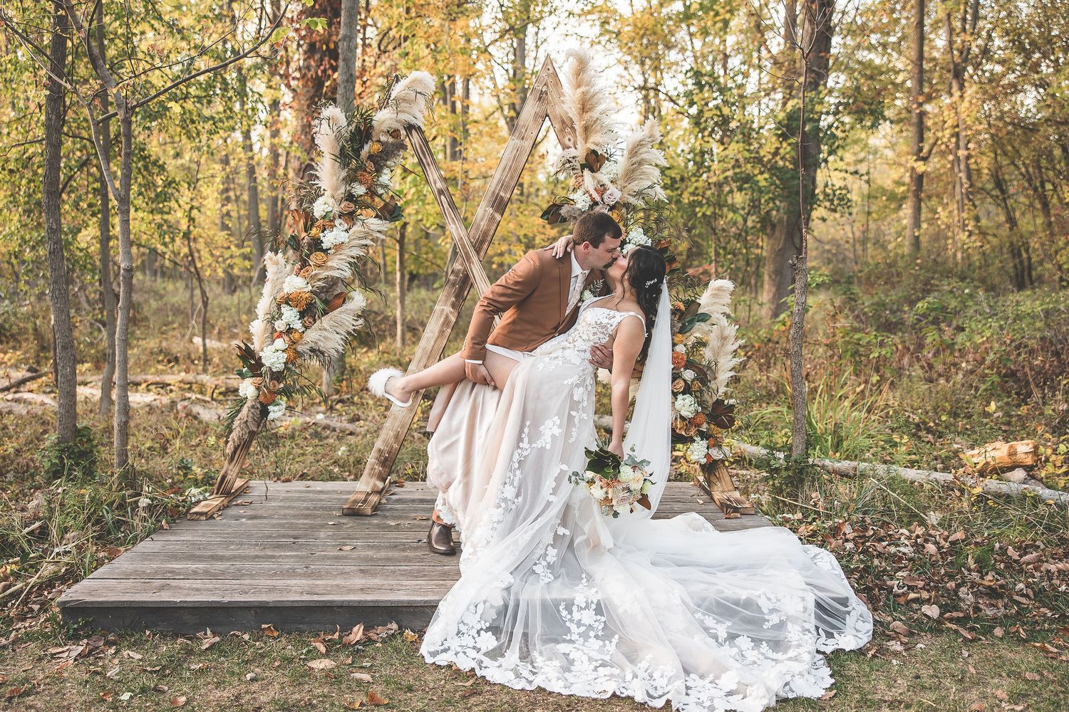 A wedding couple walks through a wooded area with sunlight streaming through autumn trees.