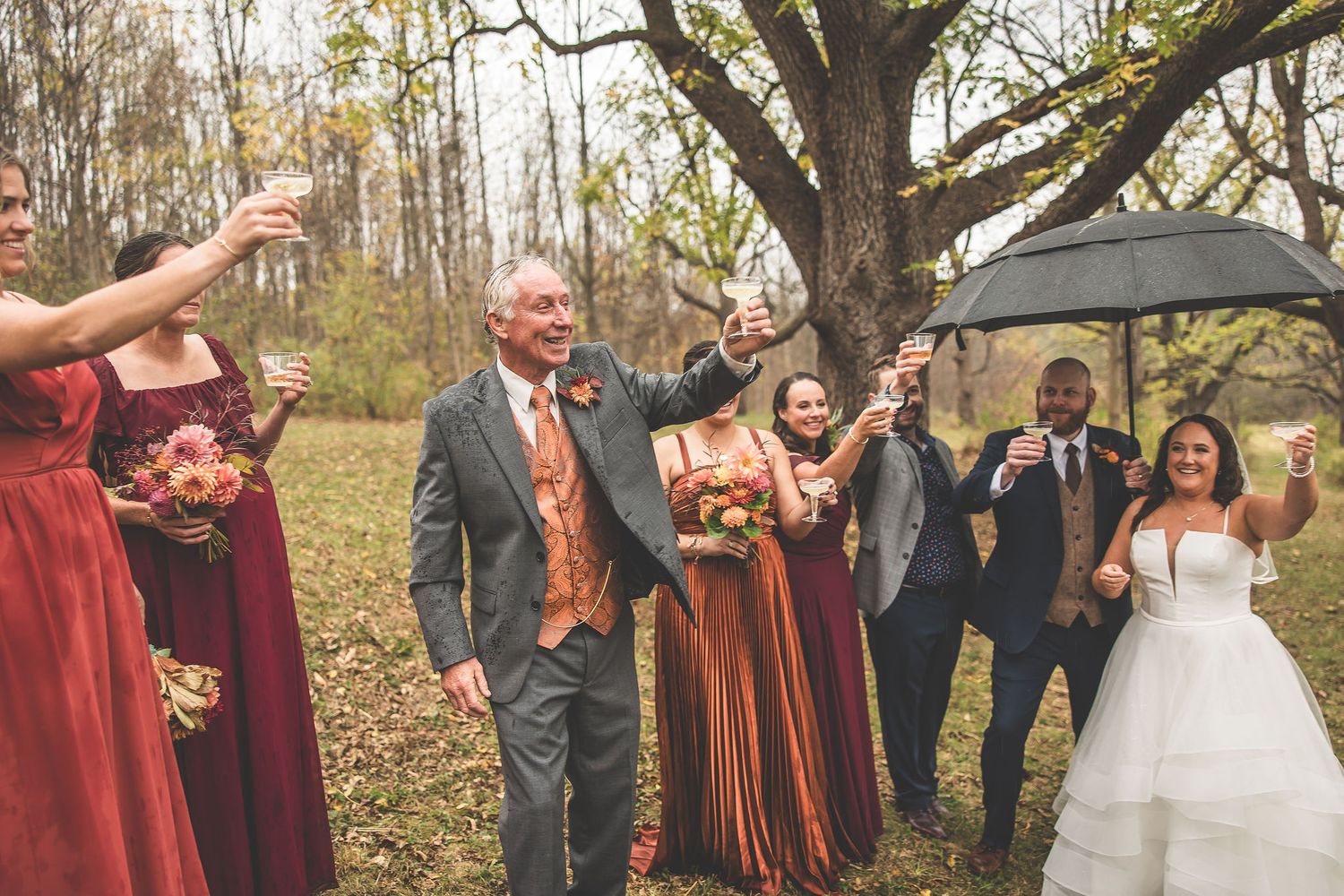 Wedding party celebrates with umbrellas during autumn outdoor ceremony.