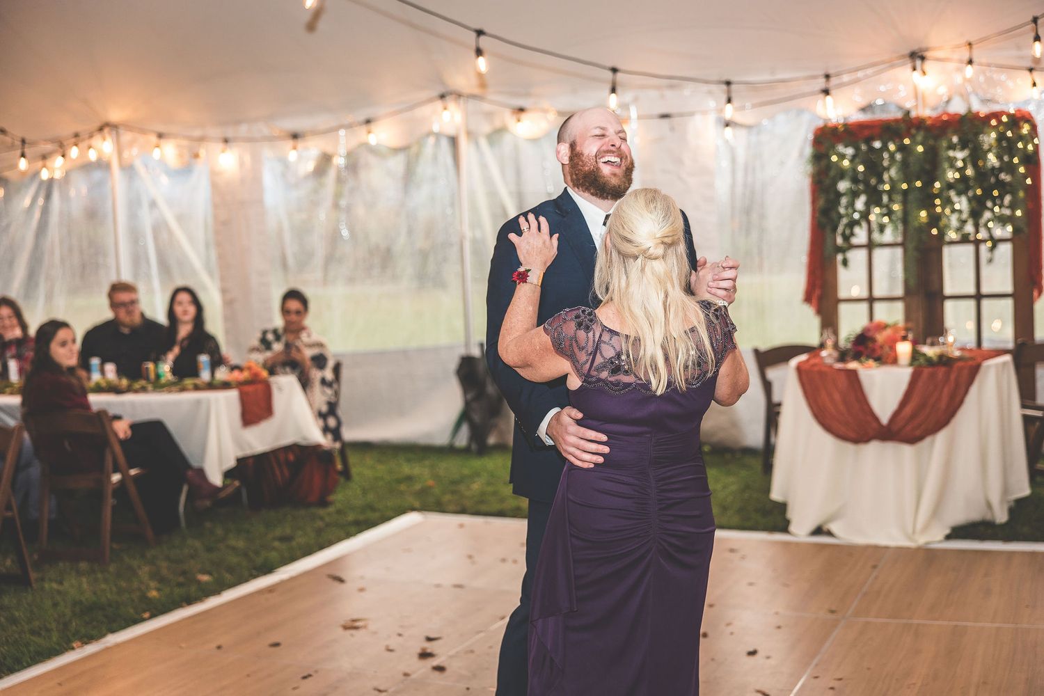 Wedding celebration in a tent decorated with string lights and white draping.