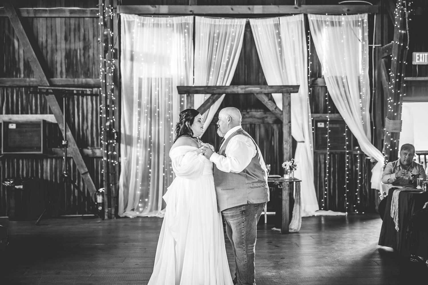 Black and white photo of a barn wedding reception with elegant draping and decorative lighting.