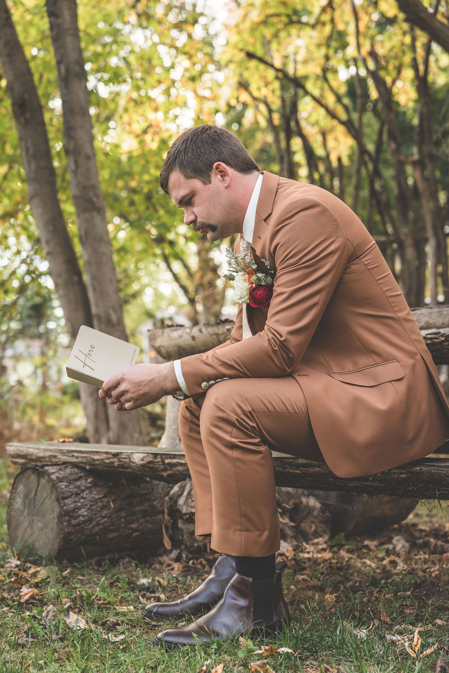 Person in brown suit sits on fallen log in autumn forest while reading.