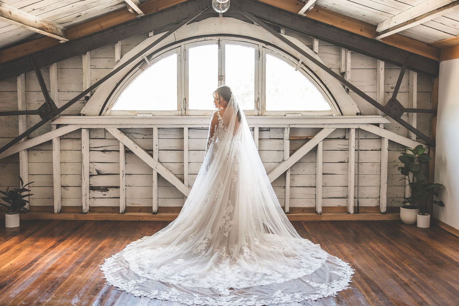 Wide angle shot of bride in cathedral length veil standing in rustic wooden attic space.