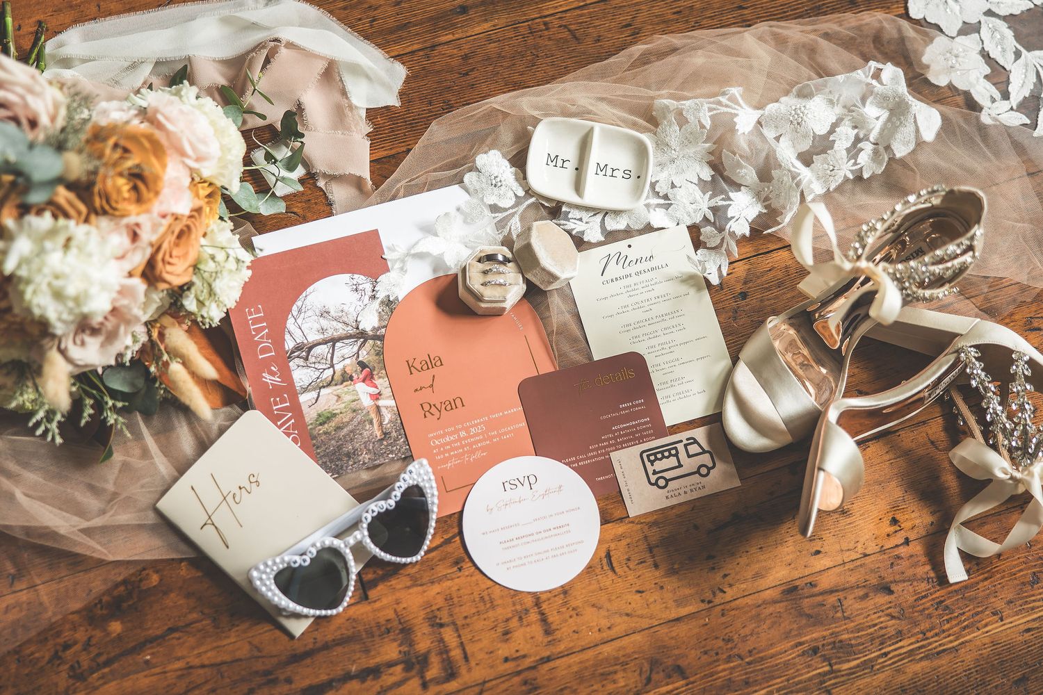 Wedding details including sunglasses, rings, and stationery arranged artistically on wooden surface.
