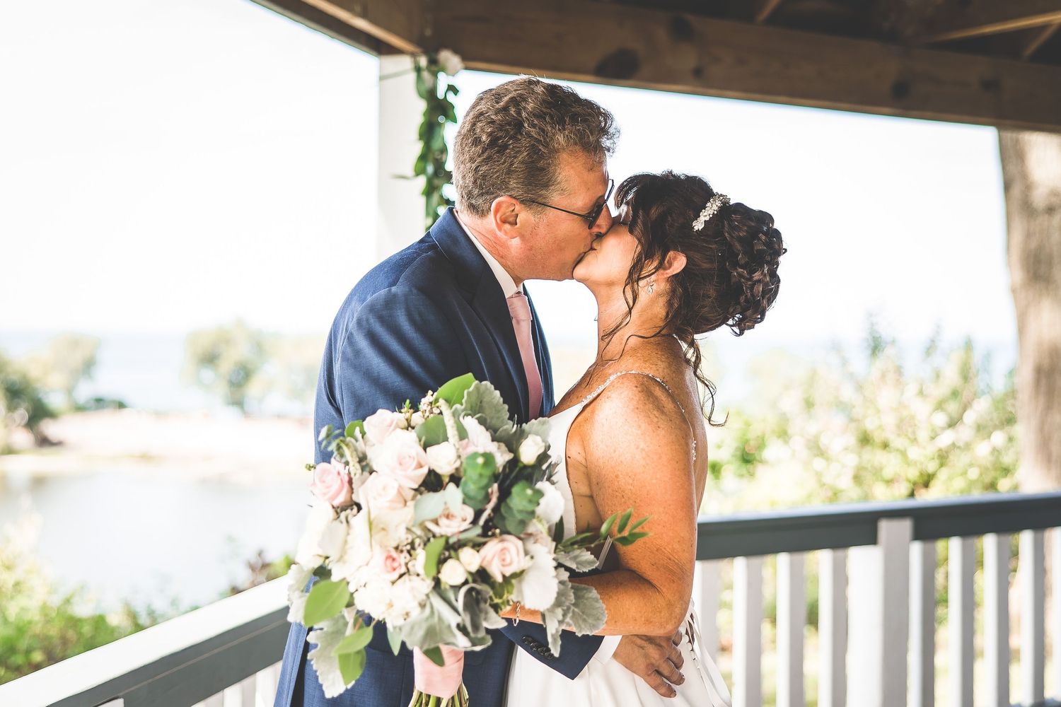 Bride and groom share tender moment during first look on wooden deck with scenic backdrop.