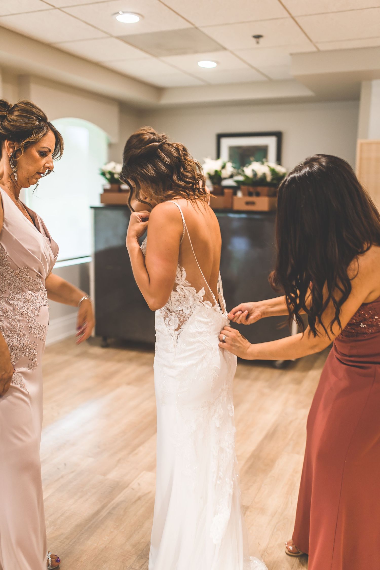 Wedding party in white and burgundy dresses preparing in a room with wooden floors.