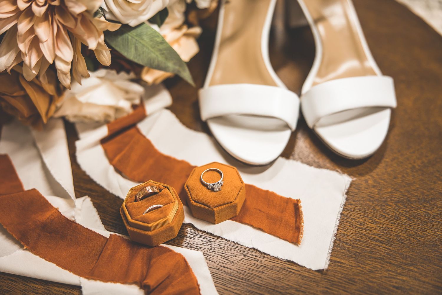 Wedding accessories including brown leather shoes and floral decorations arranged on wooden surface.