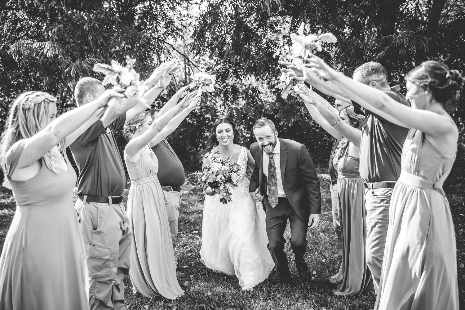 Black and white photo of wedding party creating tunnel formation for couple.