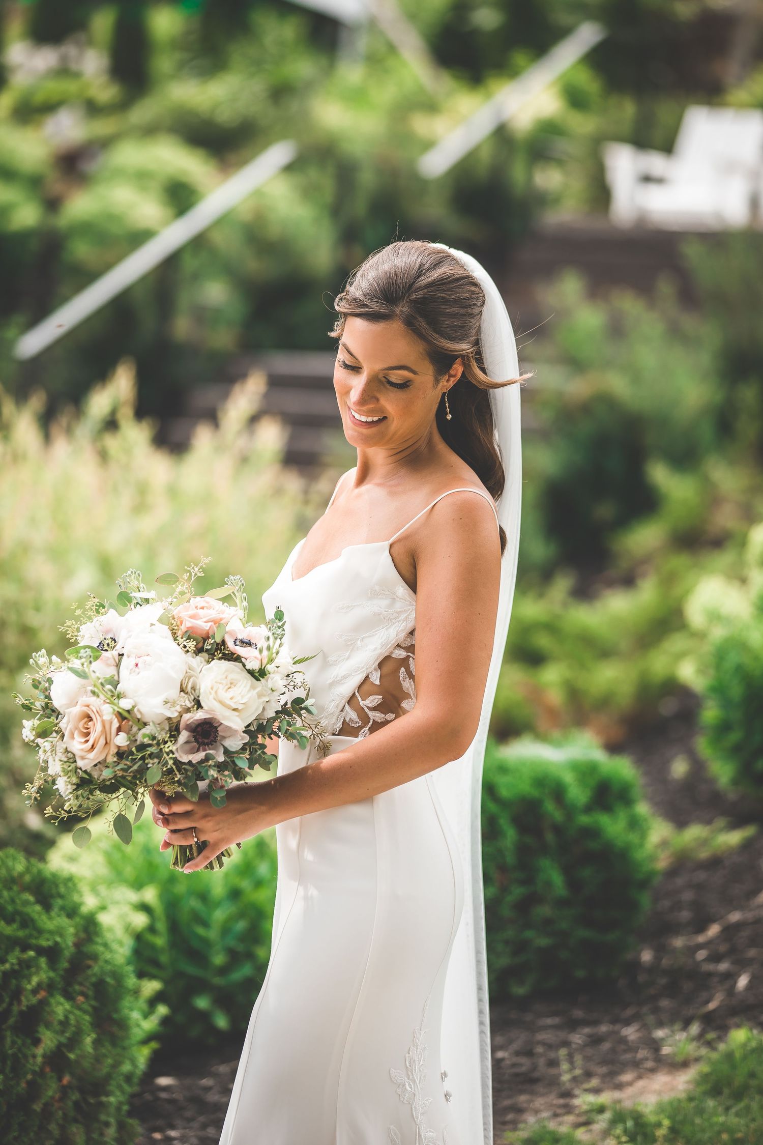 Bride holding a romantic bouquet of white and blush flowers poses in a garden setting.