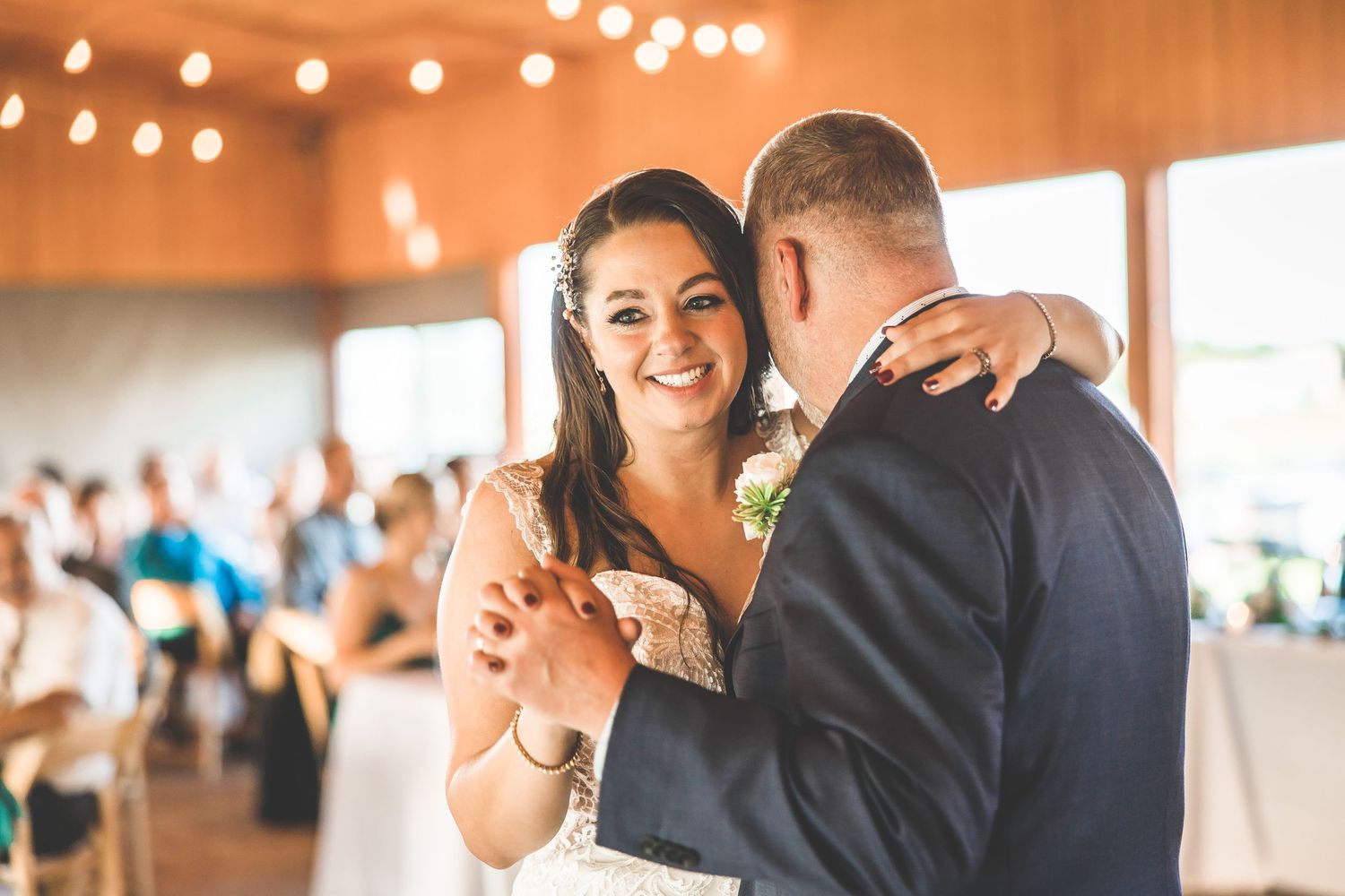 Couple dances under warm lighting at their wedding reception with string lights glowing above.