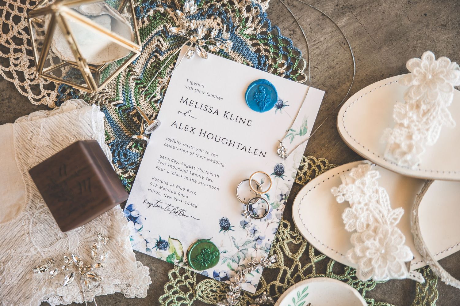 Wedding invitation with blue floral design displayed alongside rings and lace details.