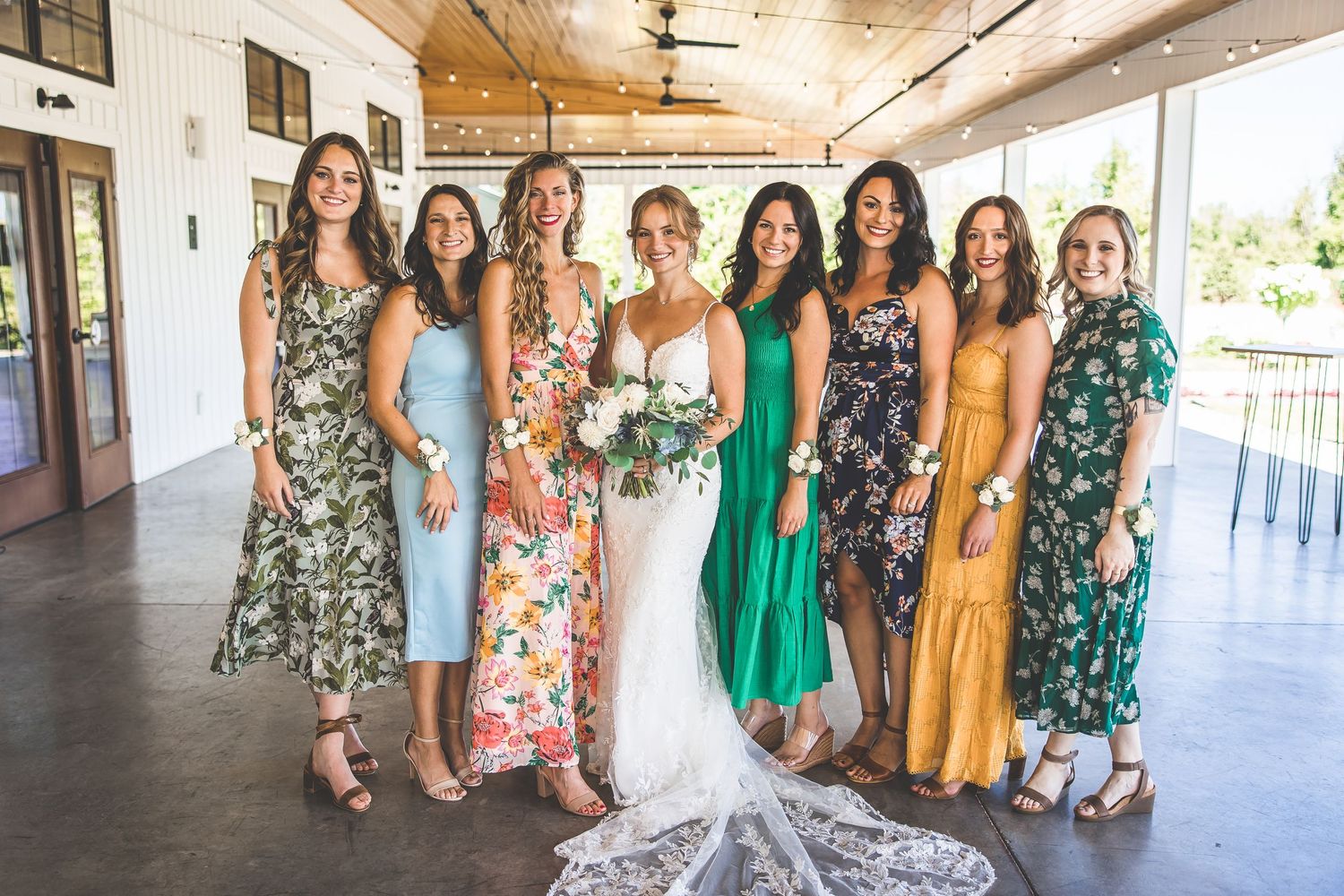 Group photo showing bridesmaids wearing colorful floral and solid dresses standing together at a venue.