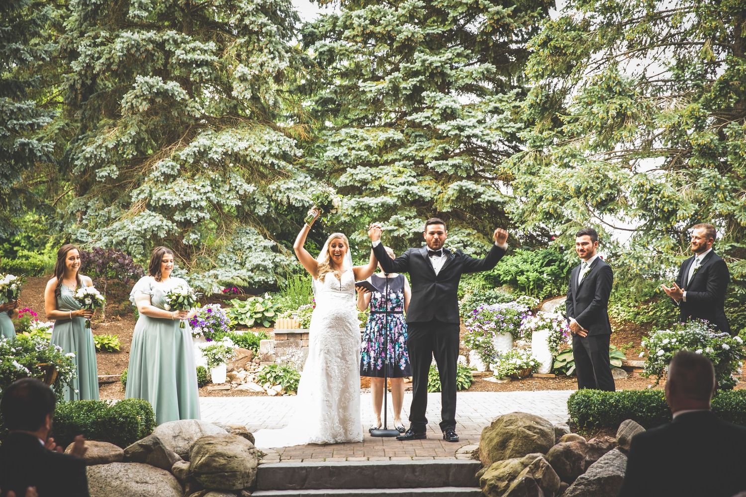 Wedding party celebration in an outdoor garden venue with natural stone features.