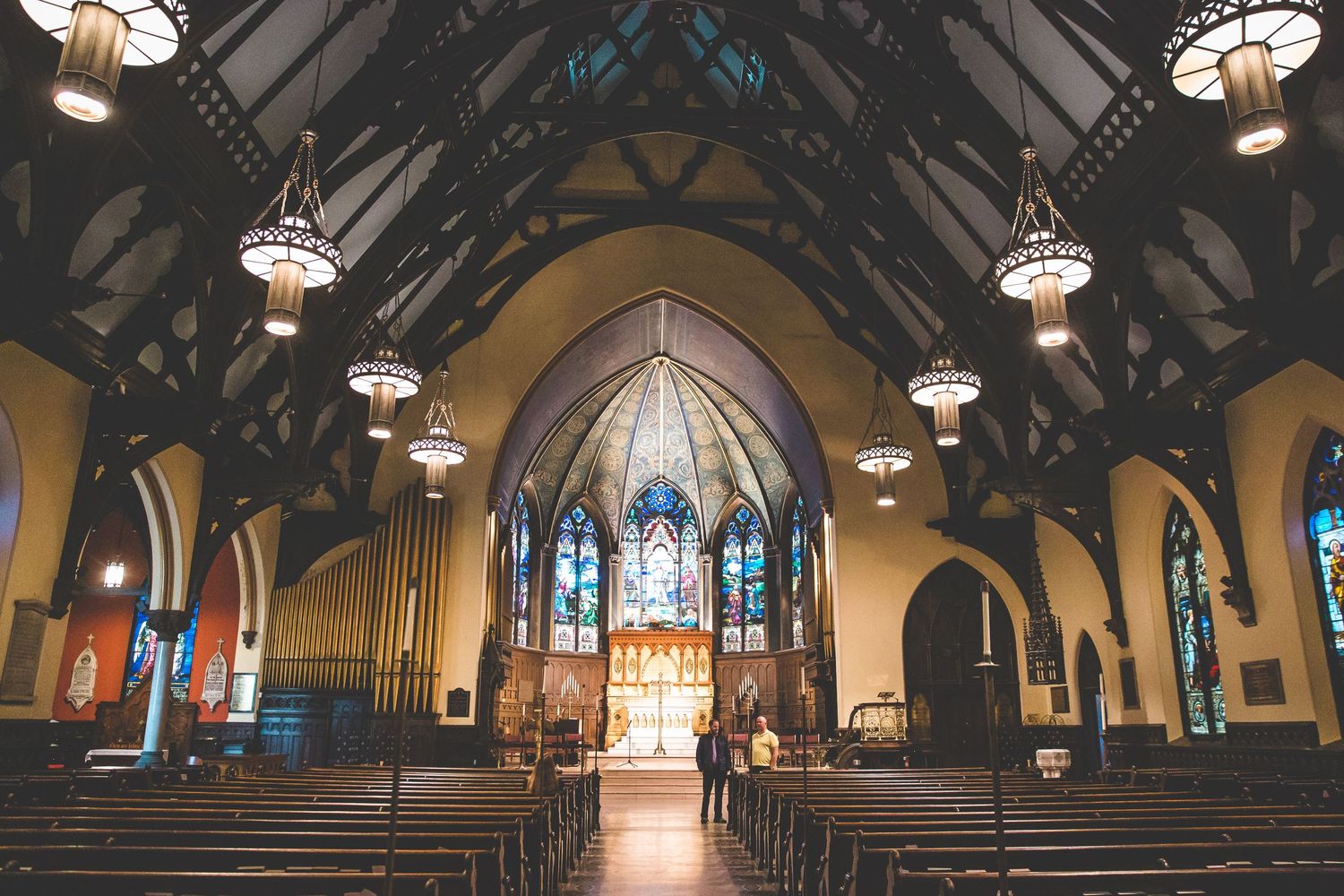 Interior panorama of a gothic church sanctuary with vaulted ceilings and ornate chandeliers.