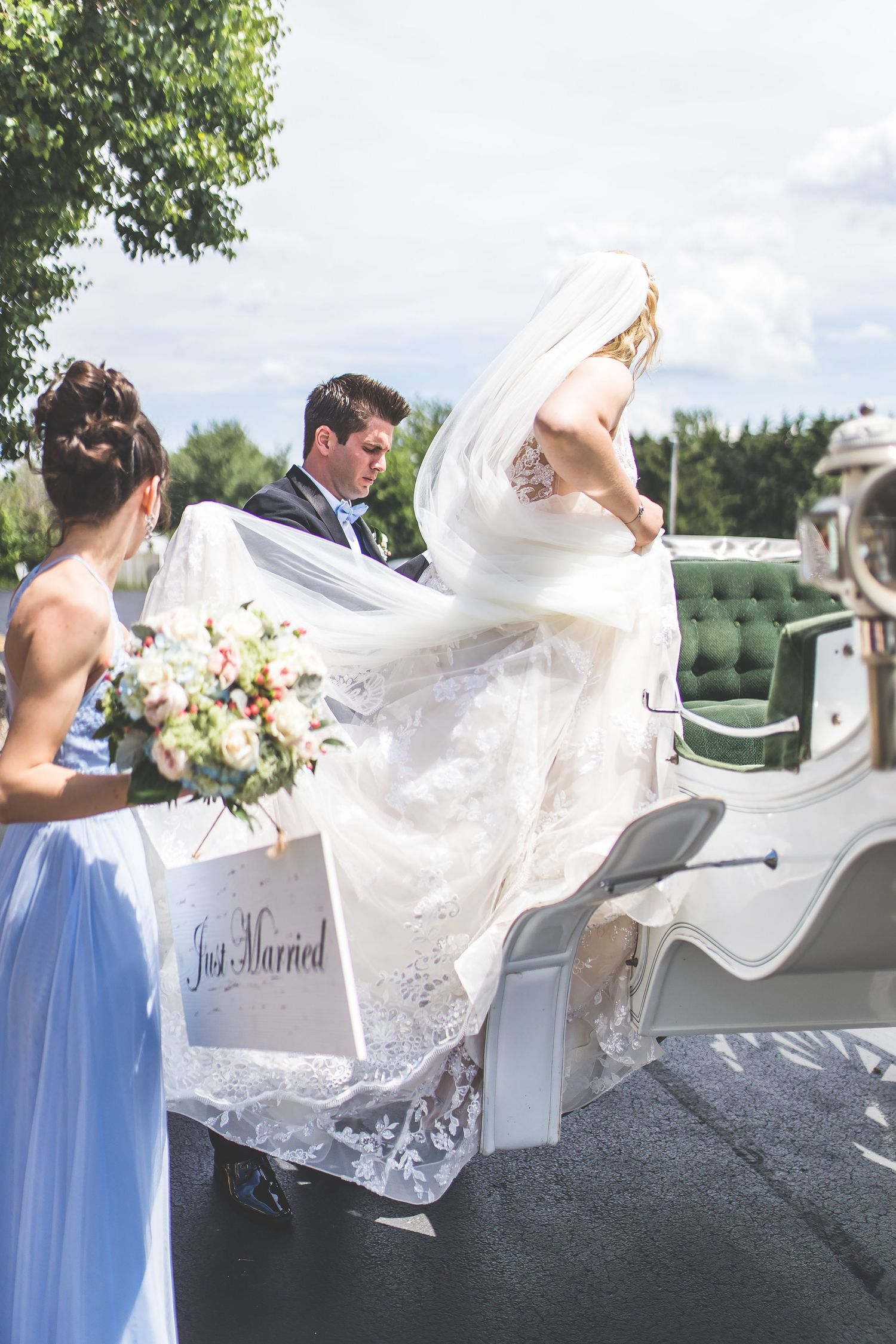 Bride in flowing white dress climbing into ornate white carriage with 'Just Married' sign.