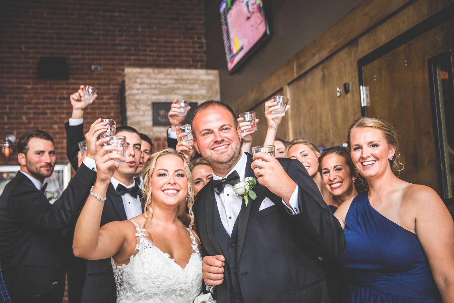 Wedding party dancing and celebrating with drinks at an indoor reception venue.