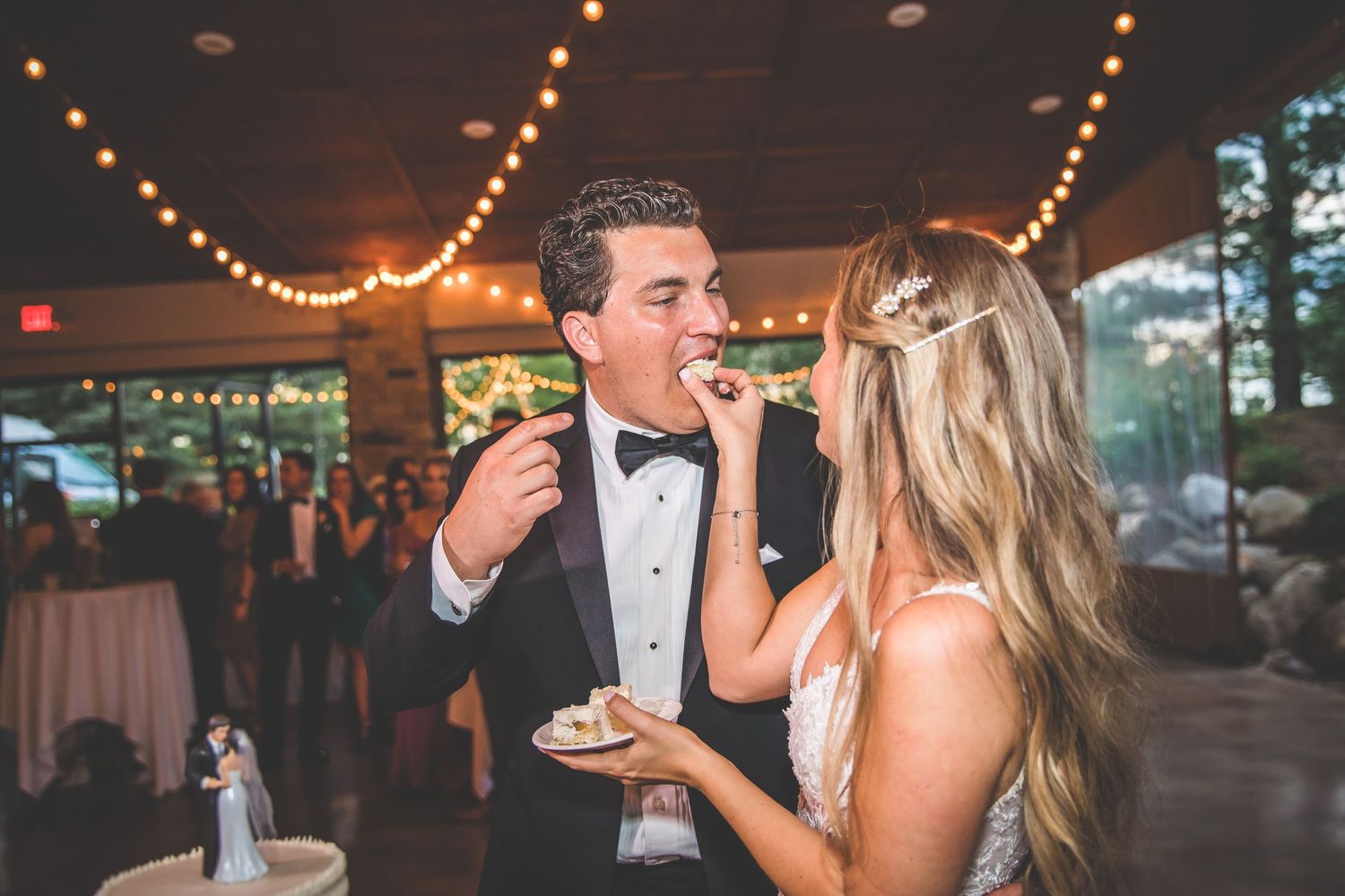 Wedding reception guests dancing and celebrating under warm string lights at an indoor venue.