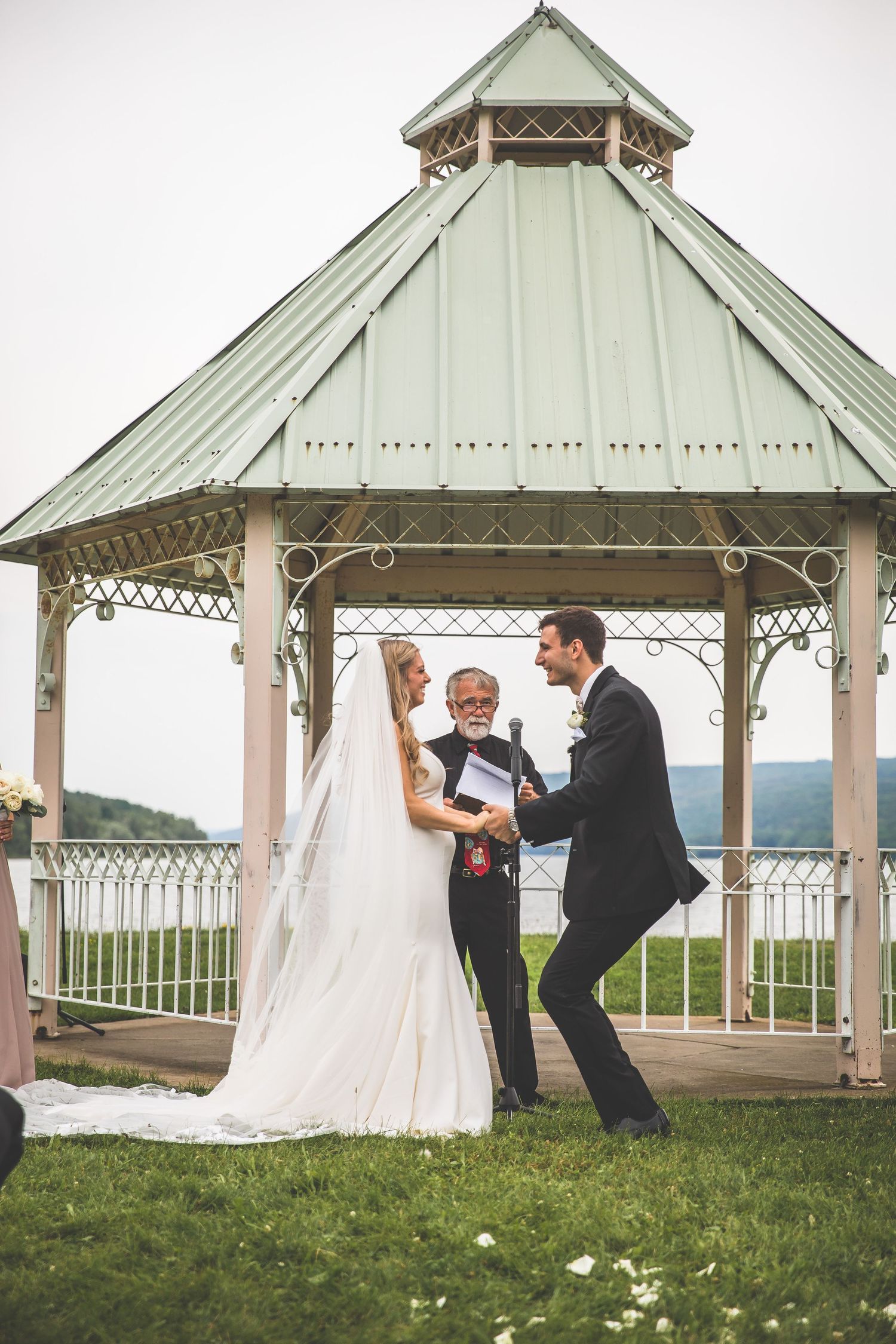 Wedding ceremony in vintage-style white gazebo surrounded by green grass and mountains.