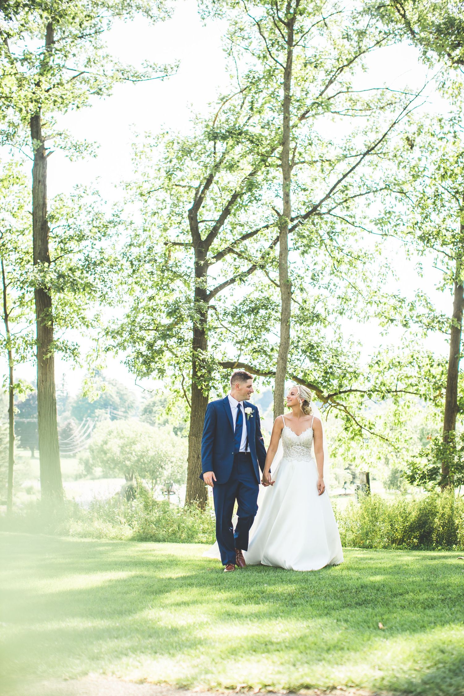Newlyweds walking together through a sunlit grove of trees.
