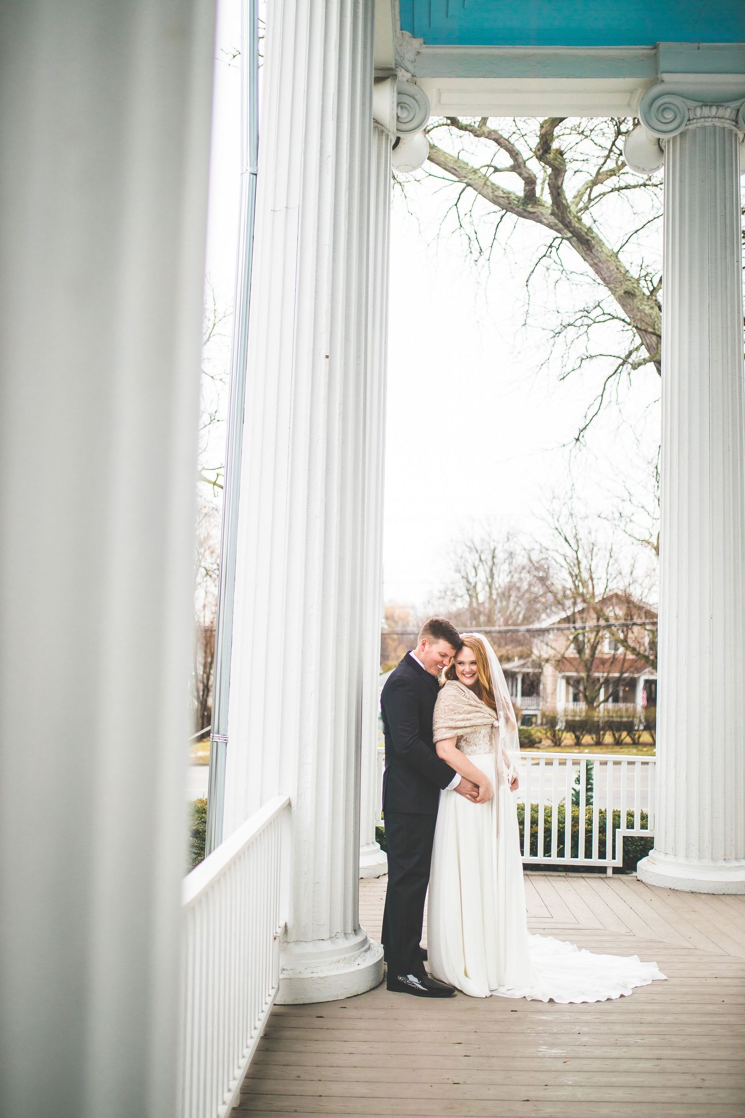 Wedding couple shares romantic moment between classic white columns on porch.