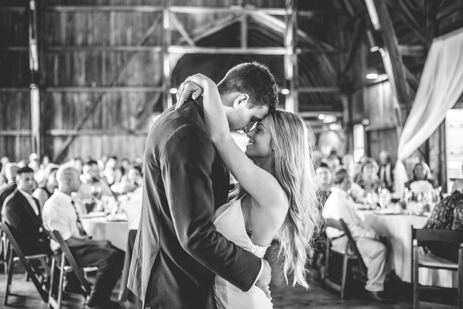 Black and white photograph of romantic dance in rustic barn reception venue.