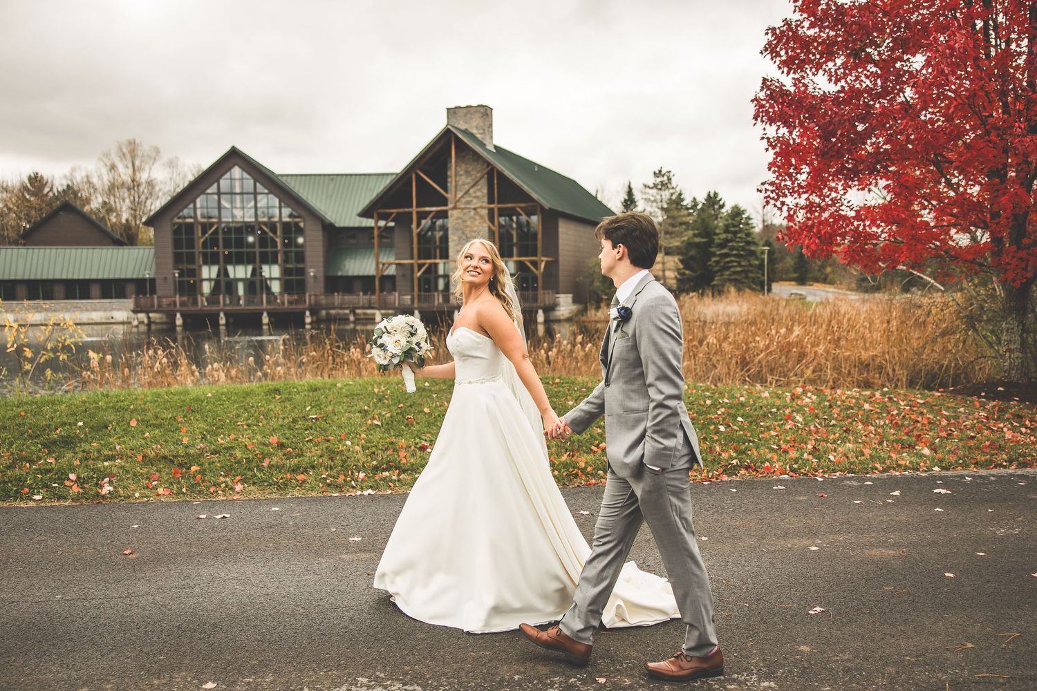 Elegant wedding photography session with rustic buildings and red autumn trees in the background.
