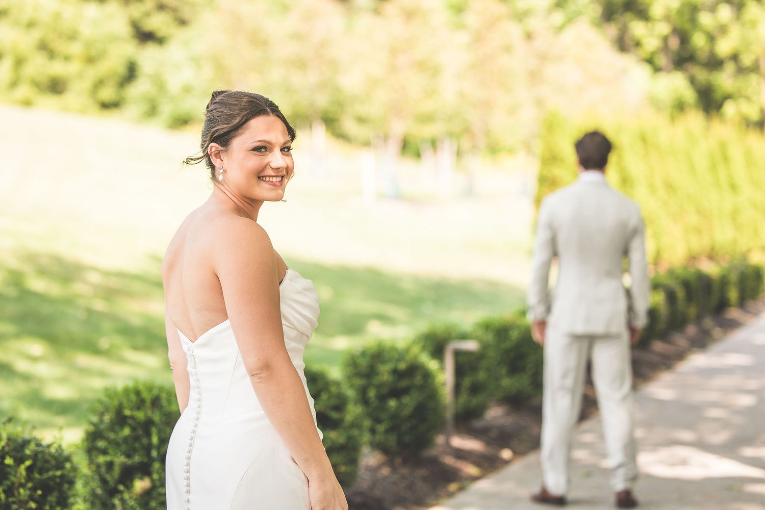 Wedding couple shares a playful first look moment on a sunlit garden path.