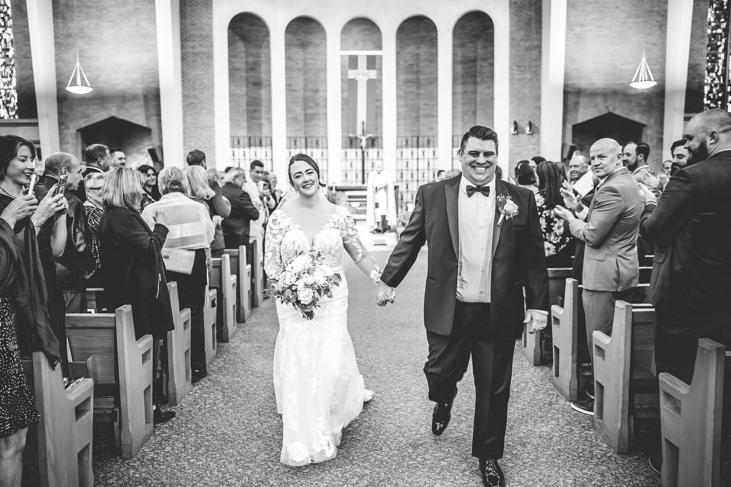 Wedding procession moving through church aisle with guests looking on from wooden pews.