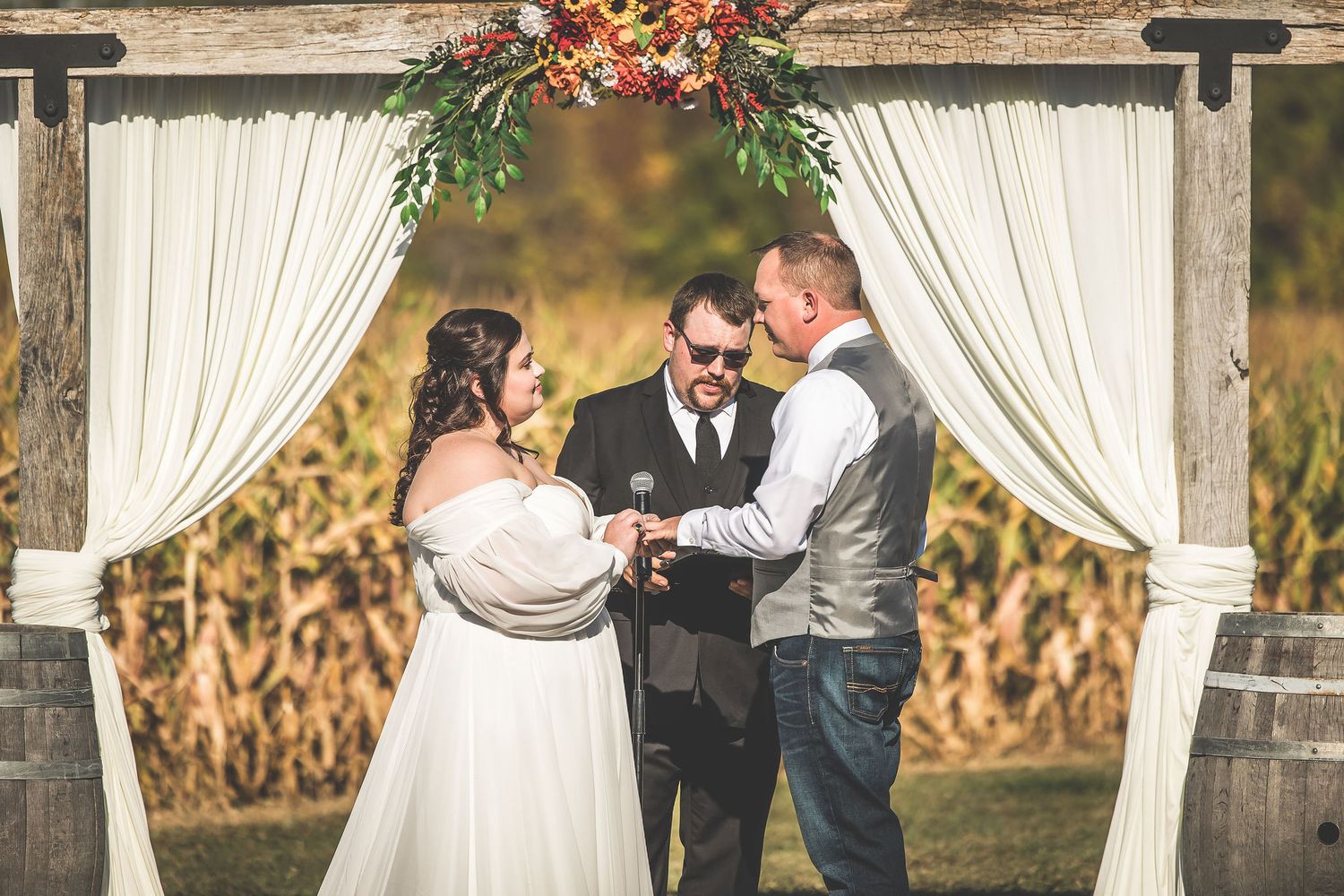 Elegant outdoor wedding setup with white draped columns and fall floral arrangements against a rustic backdrop.
