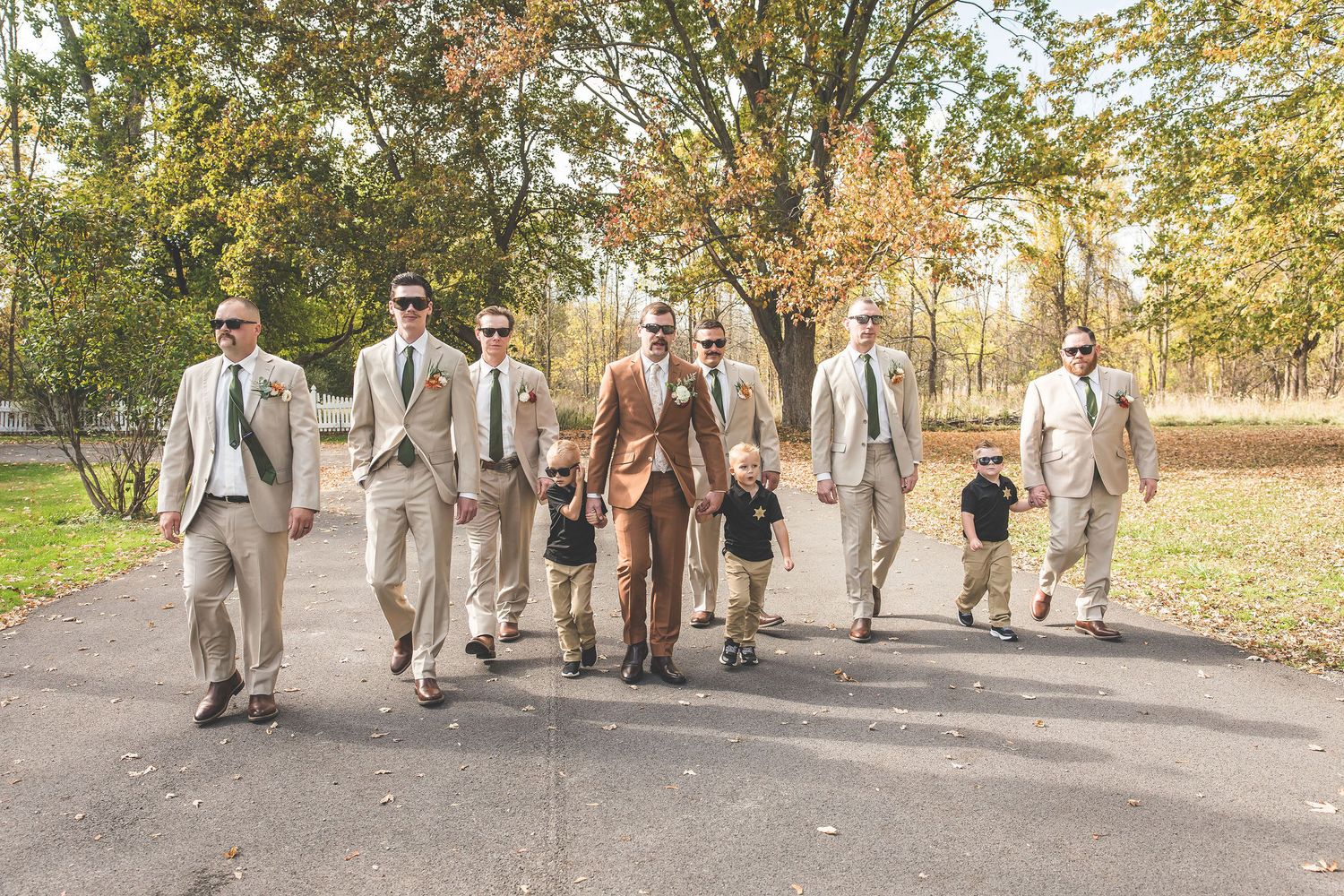 Wedding party walks together on path through autumn trees wearing earth-toned attire.