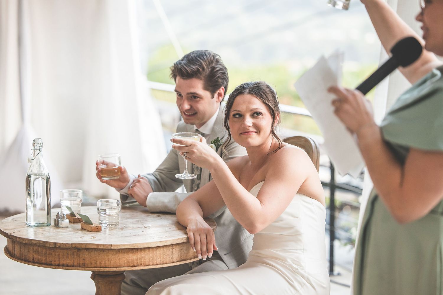 Newlyweds share drinks and laughter at their reception table.