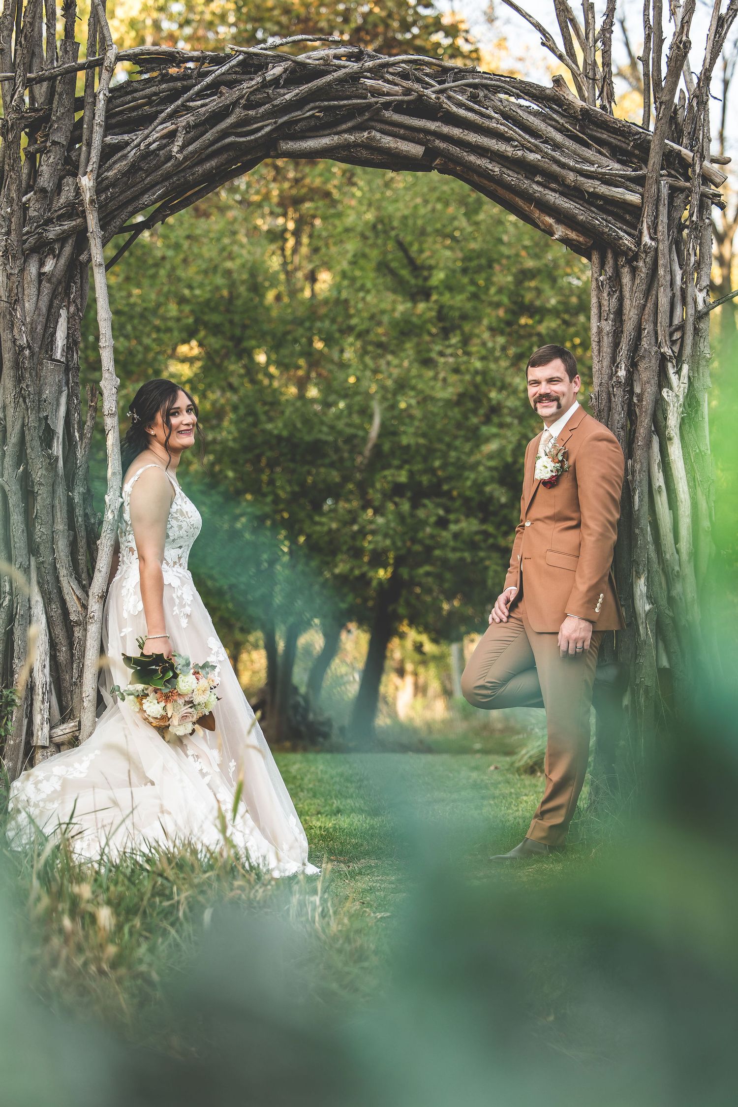 Wedding couple poses among trees with dreamy green bokeh effect in outdoor setting.