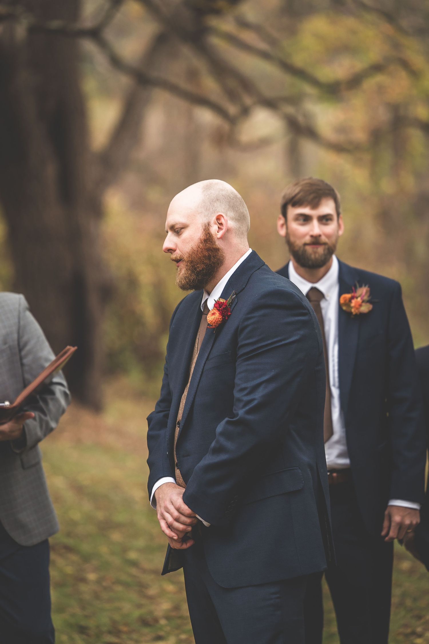 Groomsmen in navy suits and formal attire gather outdoors during autumn wedding.