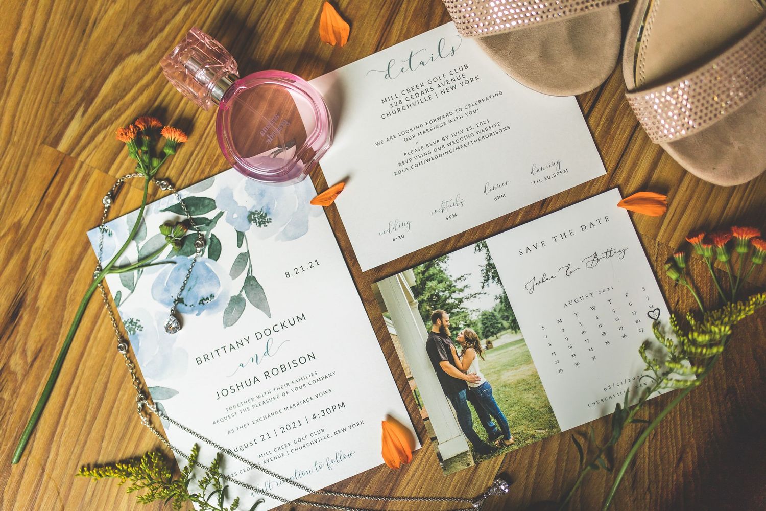 Wedding invitations and stationery with floral designs laid out on wooden surface.
