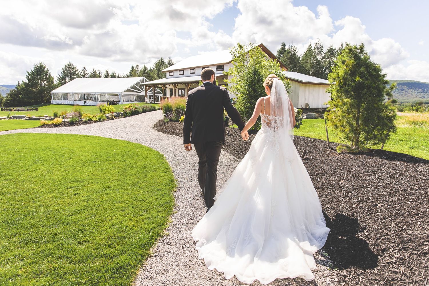 A couple walks along a curved path on their wedding day with mountains in the distance.