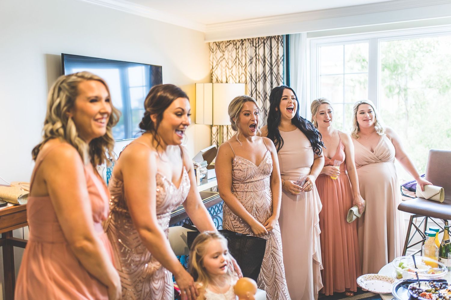 Wedding party wearing pastel dresses gathered in an elegant room for photos.