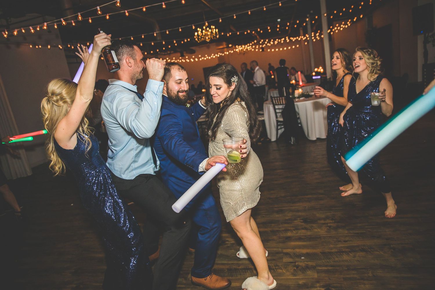 Dance floor filled with celebrating wedding guests under warm string lighting.
