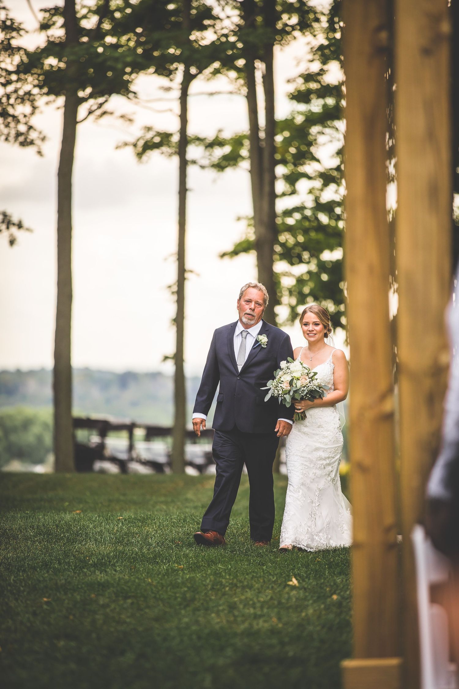 Wedding ceremony processional between wooden pillars in outdoor setting.