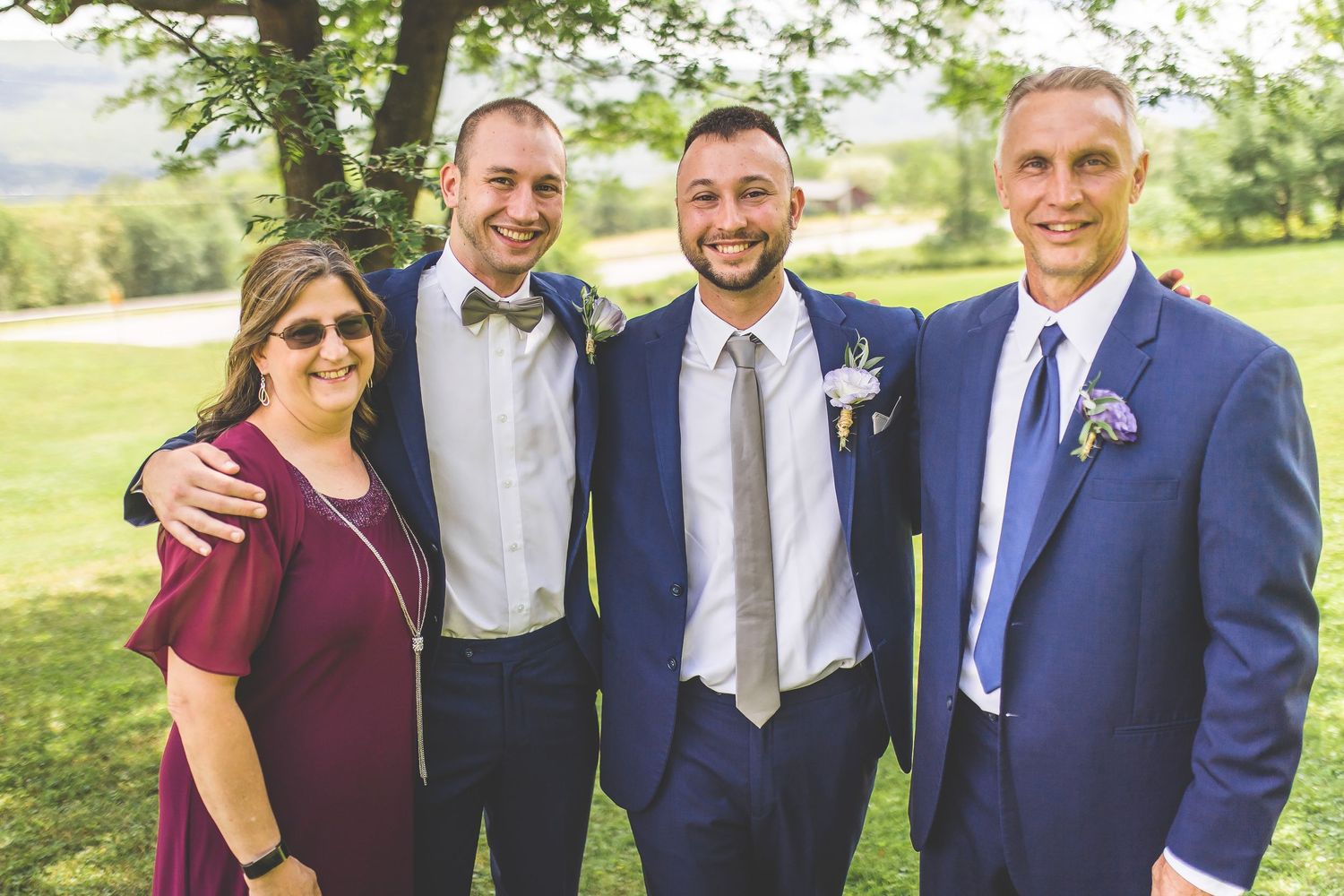 Wedding party members gather for casual group photos on sunny hillside.