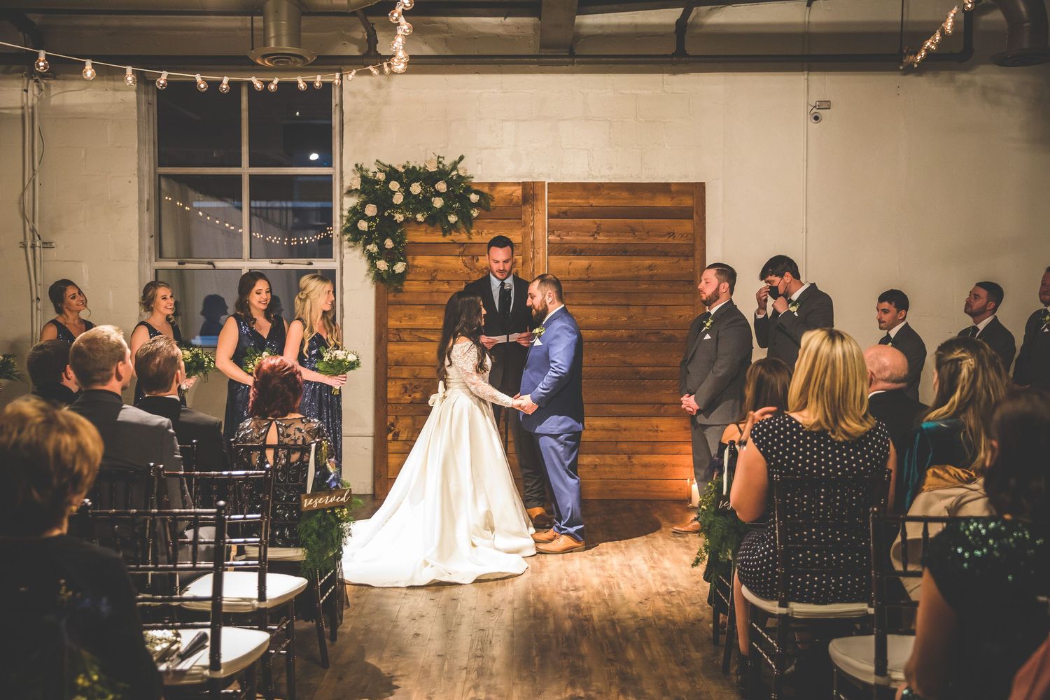 Panoramic view of a wedding reception with string lights and wooden wall accents.