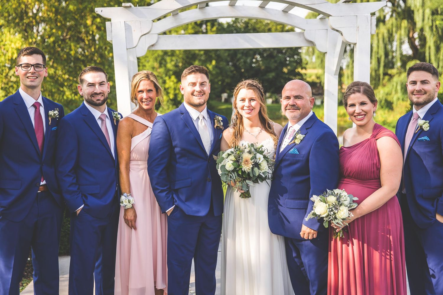 Large wedding party group photo featuring burgundy and navy color scheme under an outdoor pergola.