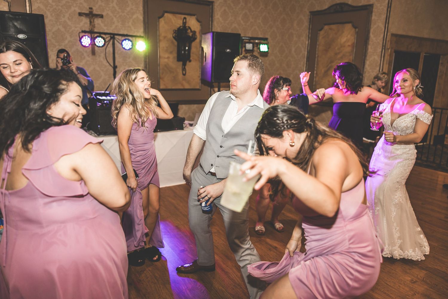 Wedding party dancing and celebrating with purple lighting effects in a ballroom.