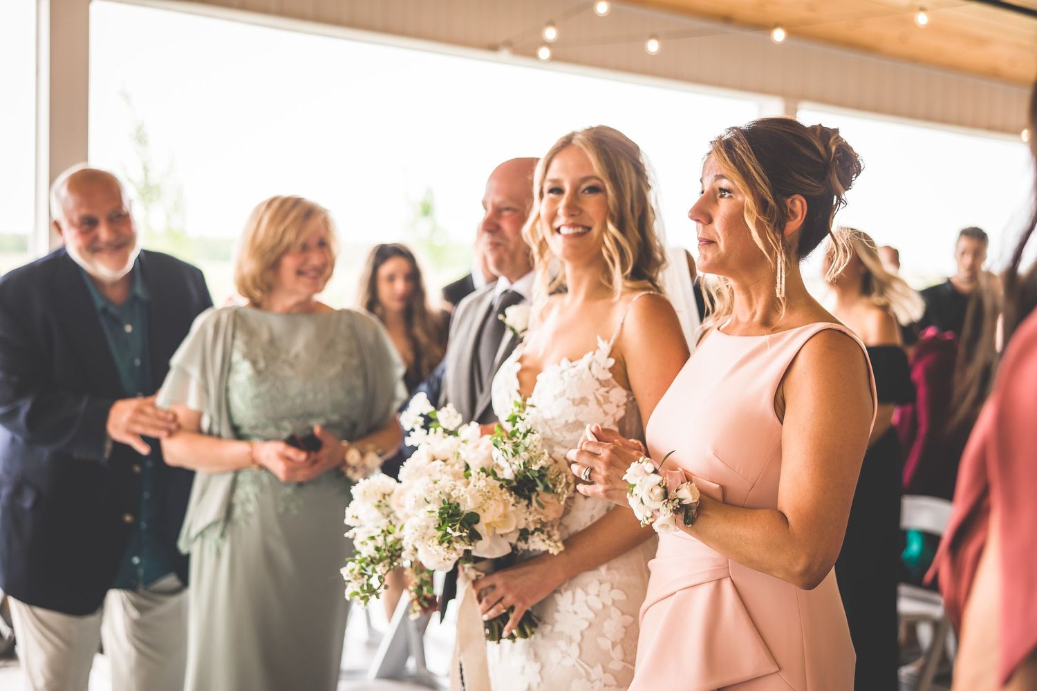 Wedding party smiles during ceremony in sunlit venue with floral arrangements.