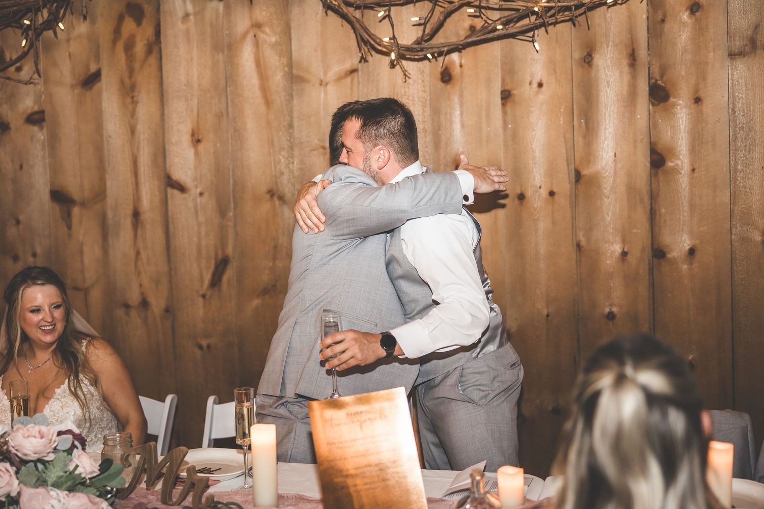 Two people embracing during an emotional moment at a wedding reception in a wooden barn setting.