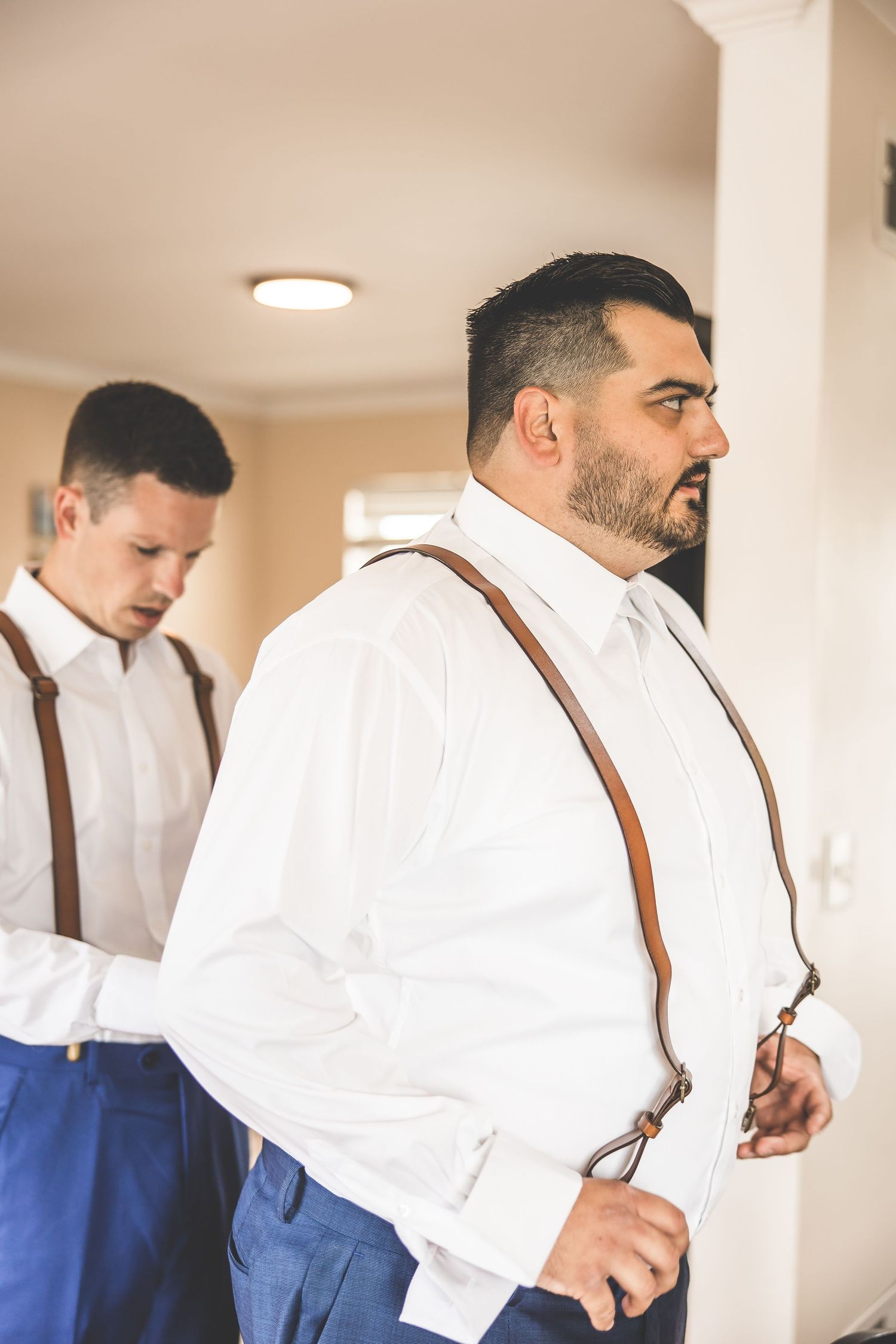 Groomsmen adjusting suspenders and getting ready in white shirts.