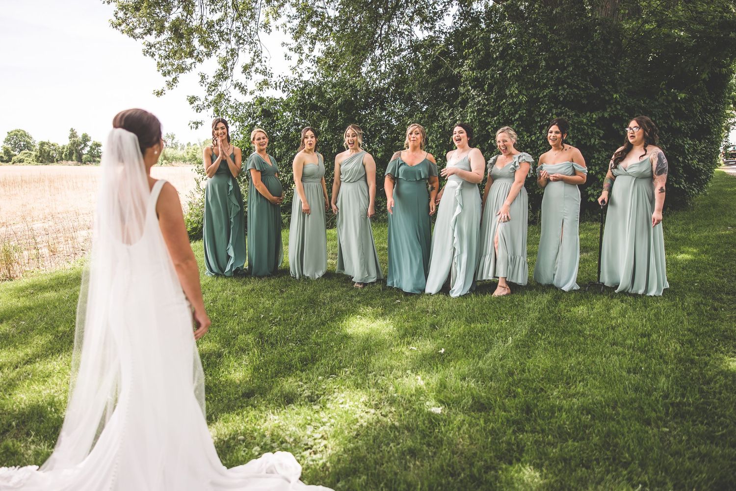 Bridesmaids in mint green dresses pose together outdoors on a sunny day.